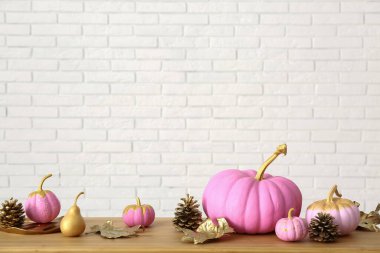 Sonbahar yapraklı pembe balkabakları ve beyaz tuğla duvarın yanındaki ahşap masada koniler.