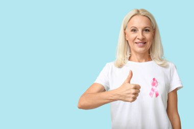 Mavi arka planda pembe kurdeleli olgun bir kadın. Göğüs kanseri farkındalığı konsepti