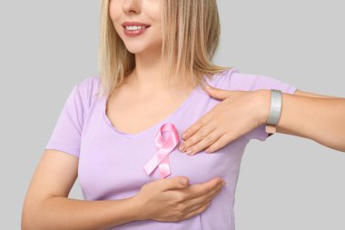 Gri arka planda pembe kurdeleli genç bir kadın. Göğüs kanseri farkındalığı konsepti