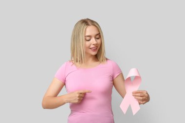 Gri arka planda pembe kurdeleli genç bir kadın. Göğüs kanseri farkındalığı konsepti