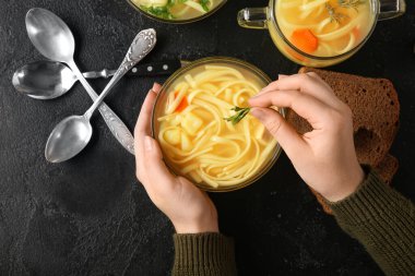 Siyah arka planda lezzetli tavuk çorbasıyla kaseye maydanoz ekleyen kadın.