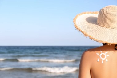 Deniz kıyısındaki genç bayanın sırtına güneş kremiyle çizilmiş.