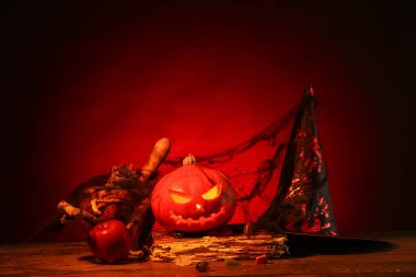 Cadılar Bayramı kompozisyonu, kriko-fener, eski kitap ve ağ ile ahşap masa üzerinde kırmızı arka plan karşı