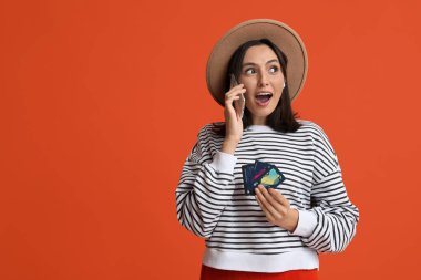 Kredi kartlarıyla kırmızı arka planda cep telefonuyla konuşan güzel genç bir kadın.