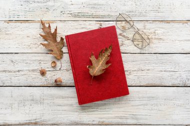 Kitap, dökülen yapraklar ve hafif ahşap arka planda gözlüklü kompozisyon
