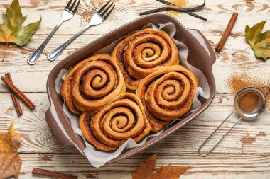 Beyaz ahşap arka planda lezzetli tarçınlı çörekler ve sonbahar yaprakları pişirmek.