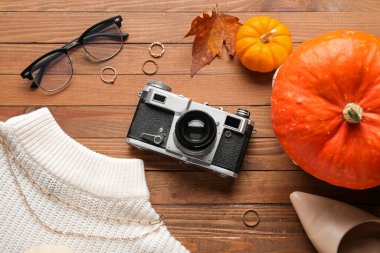 Klasik fotoğraf makinesi, kadın aksesuarları, ahşap arka planda giysiler ve balkabakları olan kompozisyon, yakın plan.