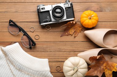 Kadın aksesuarlarından, ayakkabılarından, fotoğraf makinesinden ve ahşap arka planda sonbahar dekorundan yapılmış çerçeve, yakın plan