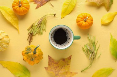 Renkli arka planda bir fincan aromatik kahve, balkabağı ve düşmüş yapraklı kompozisyon