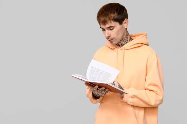 Gri arkaplan üzerine kitap okuyan dövmeli genç adam.