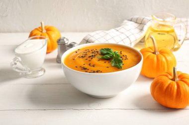 Bir kase lezzetli kabak kremalı çorba, tohumlu ve fesleğenli beyaz ahşap masa.