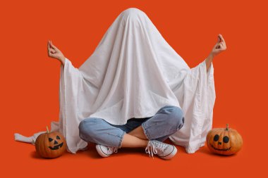 Cadılar Bayramı kostümlü kadın balkabaklı hayalet renkli arka planda oturuyor.