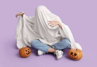 Cadılar Bayramı kostümlü, balkabaklı, leylak arka planda oturan bir kadın.