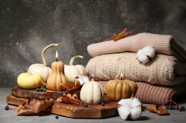 Balkabağı şeklinde yanan mumlar, pamuk çiçekleri ve gri arka planda sonbahar yapraklarıyla güzel bir kompozisyon.