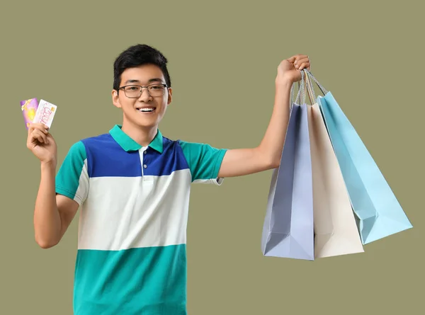 Young Asian man with gift cards and shopping bags on green background
