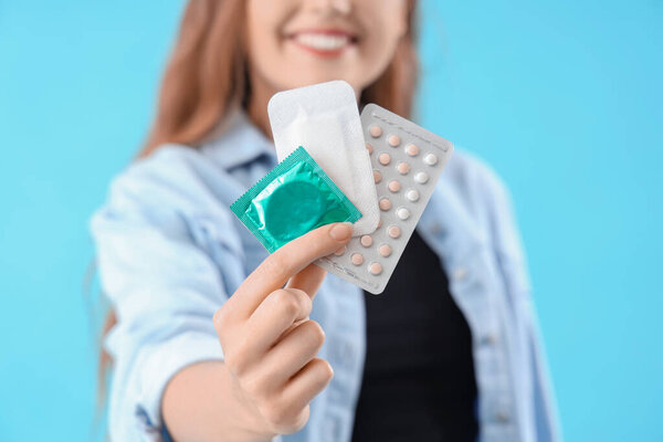 Young woman with contraceptives on blue background, closeup