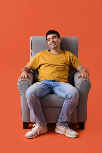 Young man sitting in armchair on red background