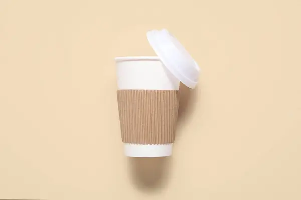 Empty takeaway paper cup with lid on beige background