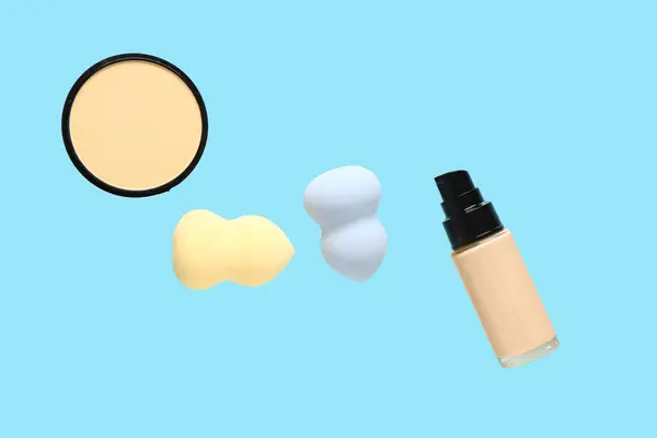 Makeup sponges, powder and liquid foundation flying on color background