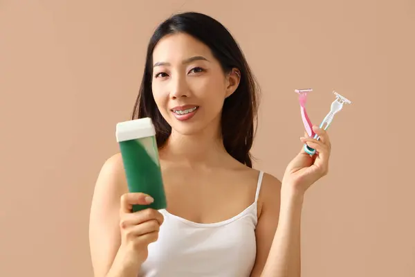 Young Asian woman with liposoluble wax cartridge and razors on beige background