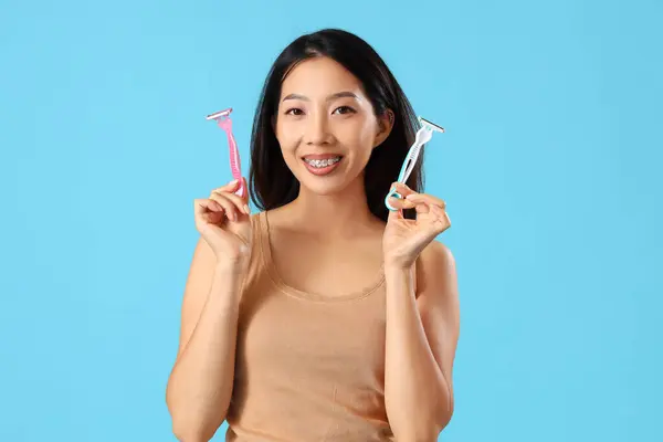 Young Asian woman with razors on blue background