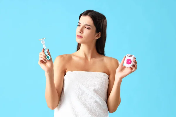 Thoughtful young woman with razor and epilator on blue background