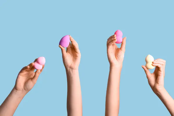 Female hands with different makeup sponges on blue background