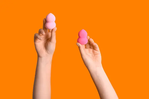 Female hands with different makeup sponges on orange background
