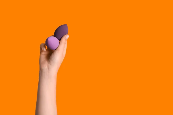 Female hand with different makeup sponges on orange background