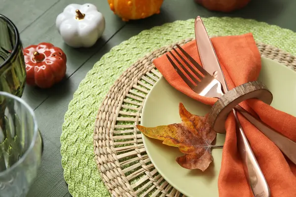 Autumn table serving with golden cutlery, pumpkins and dry leaf on green wooden table, closeup