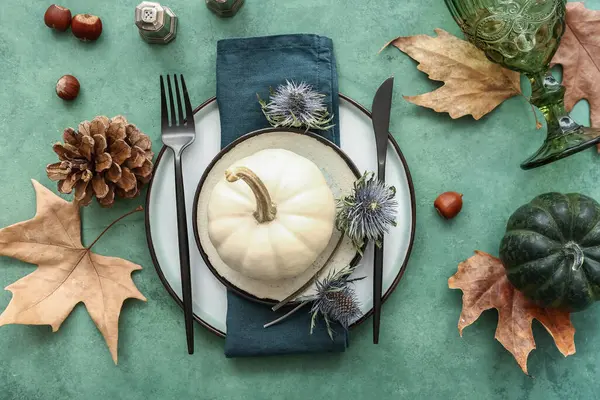 Autumn table setting with pumpkins, dried flowers and leaves on green background
