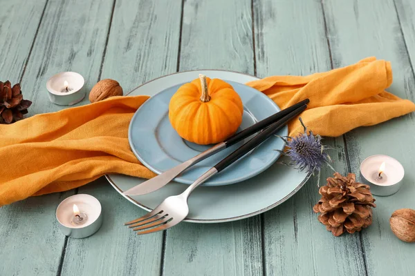 Autumn table setting with pumpkin, dried flower and burning candles on blue wooden background