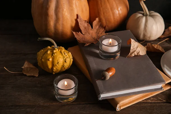 Books, autumn leaves, burning candles and pumpkins on wooden background