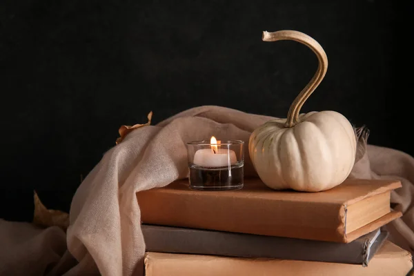 Burning candle with scarf, pumpkin and books on black background