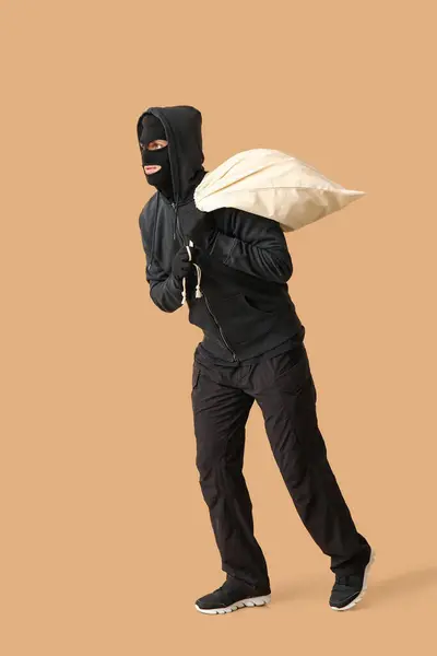 Male thief with bag on beige background