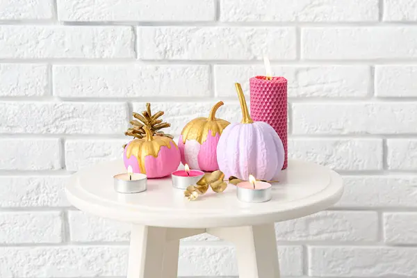 Beautiful composition with painted pumpkins and burning candles on table near brick wall