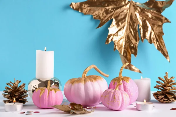 Pink painted pumpkins with golden leaves and burning candles on colorful background