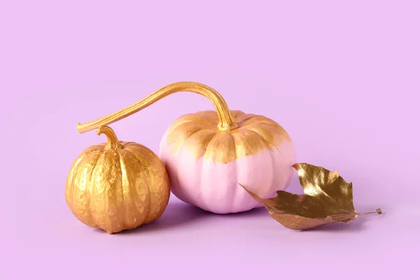 Painted pumpkins with golden leaf on lilac background