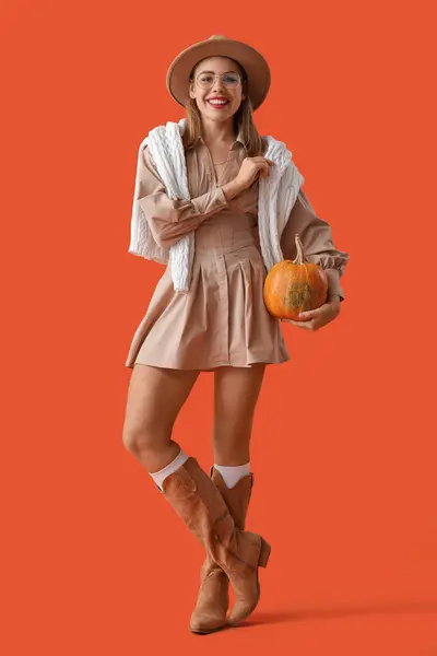 Beautiful young woman with pumpkin on orange background