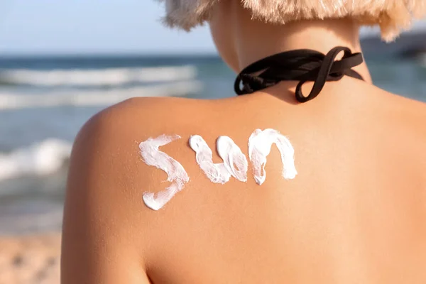 Word SUN drawn with sunscreen cream on young woman\'s back at sea resort