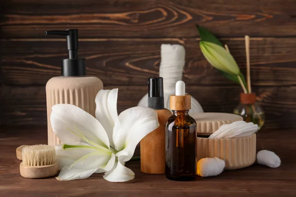 Bottles of cosmetic products, bath supplies and lily flowers on wooden background
