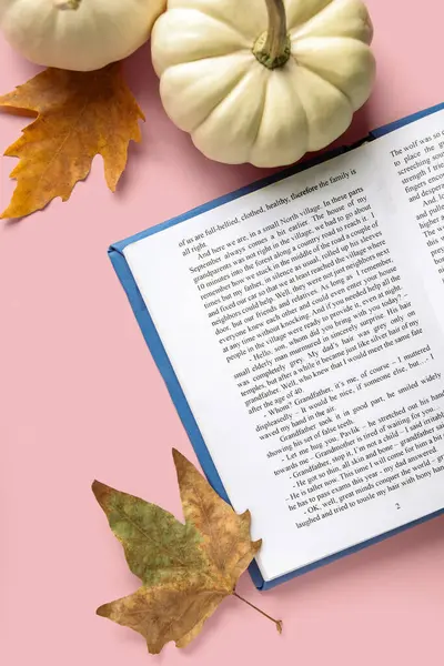 Composition with open book, pumpkins and fallen leaves on pink background