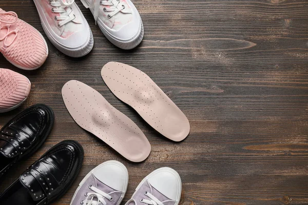 Set of different female shoes and orthopedic insoles on wooden background