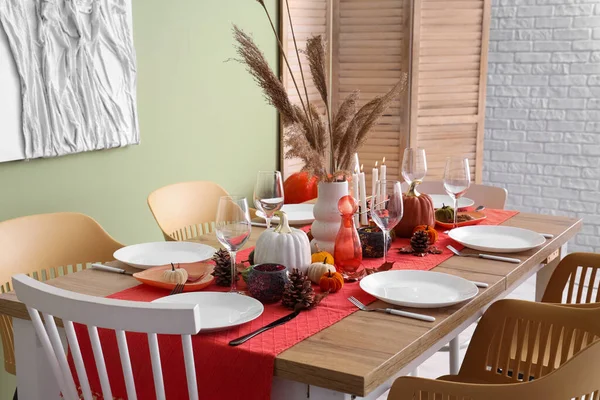 Autumn table setting with pumpkins, dry leaves and pine cones in dining room