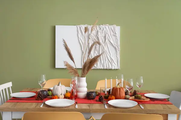 Autumn table setting with pumpkins, dry leaves and burning candles in dining room
