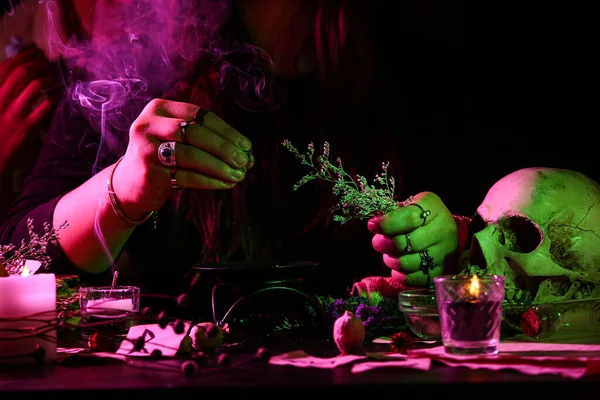 Witch with herbs at dark table, closeup