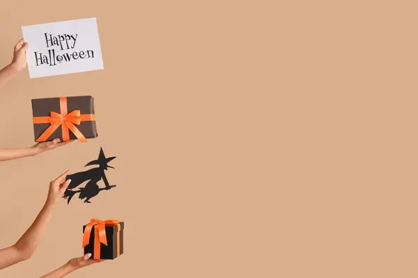 Women with Halloween gifts, paper witch and card on beige background