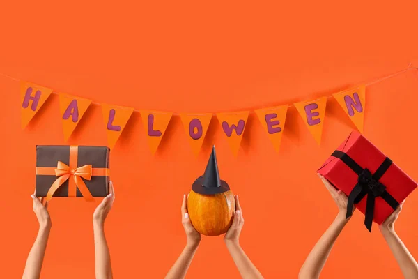 Women with Halloween gifts, pumpkin and flags on orange background