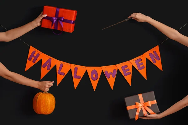 Women with Halloween gifts, pumpkin, wand and flags on dark background