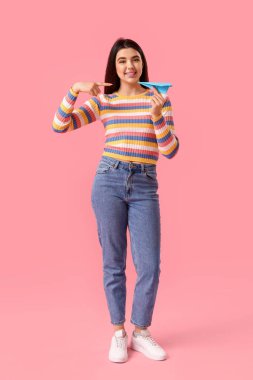 Pembe arka planda kağıt uçak gösteren genç bir kadın.